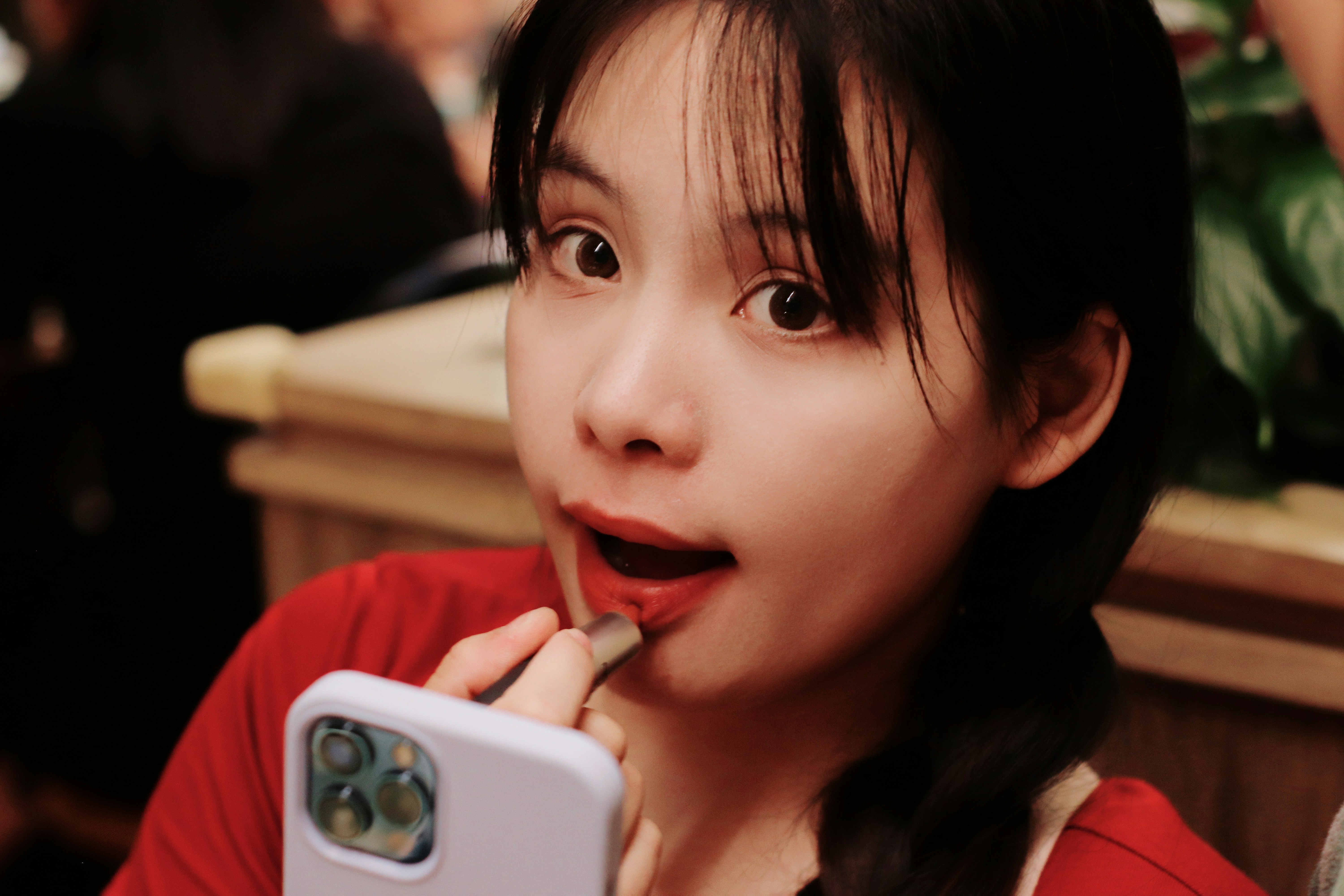 A woman is applying lipstick in a selfie.